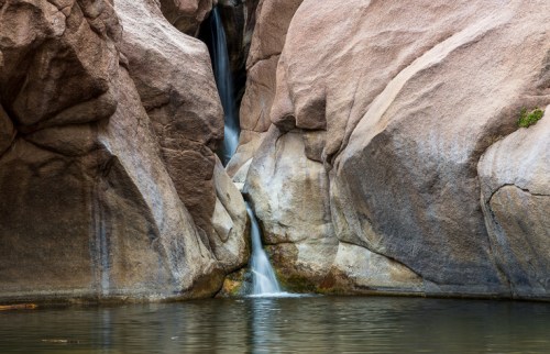 A serene waterfall cascading between large, smooth rock formations into a calm pool of water.