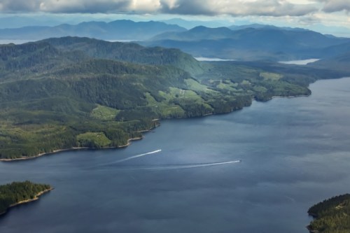 Aerial view of a serene lake surrounded by lush green mountains under a cloudy sky. Two boats are visible on the water.