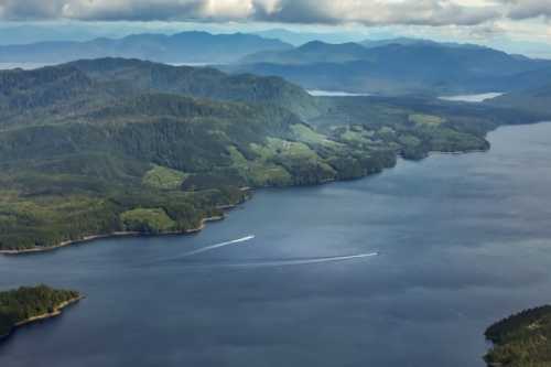 Aerial view of a serene lake surrounded by lush green mountains under a cloudy sky. Two boats are visible on the water.