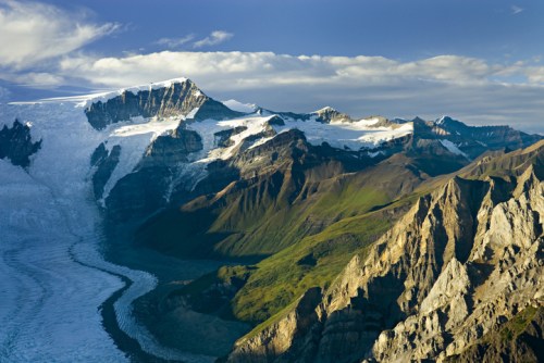 A stunning mountain landscape featuring glaciers, rocky peaks, and lush green valleys under a clear blue sky.