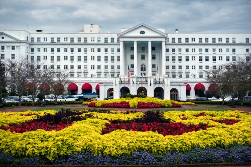 Historic hotel with a grand facade, surrounded by colorful flower beds and a cloudy sky.