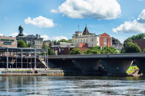 A scenic view of a river with buildings and trees along the shore under a partly cloudy sky.