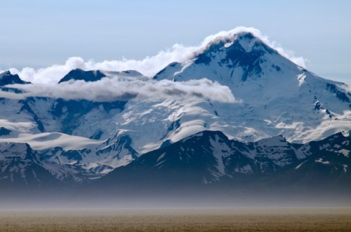 Snow-capped mountain peaks rise above a misty landscape, with clouds gently enveloping the summit.