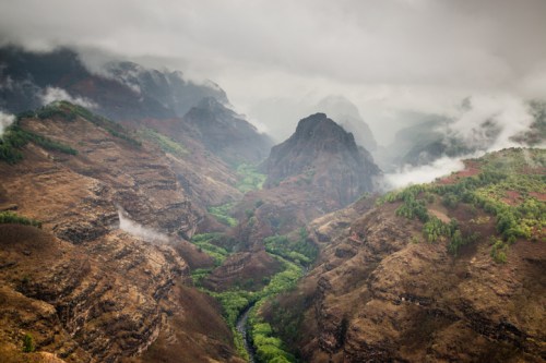 A misty mountain landscape with steep, rugged terrain and a lush green valley winding through the hills.