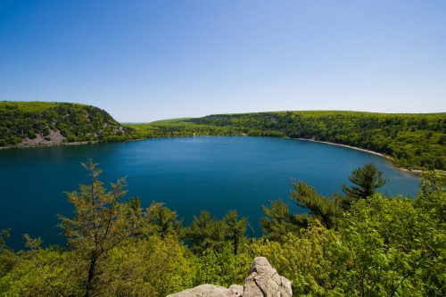 A serene blue lake surrounded by lush green trees under a clear blue sky.