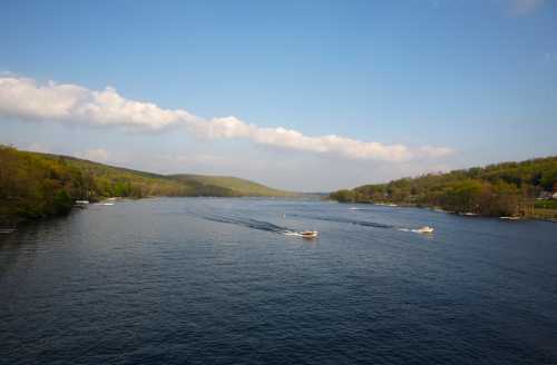 A serene river scene with boats gliding through calm waters, surrounded by lush green hills under a blue sky.