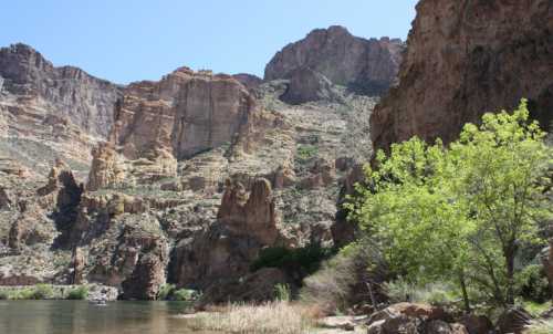 A scenic view of a river surrounded by towering cliffs and lush greenery under a clear blue sky.