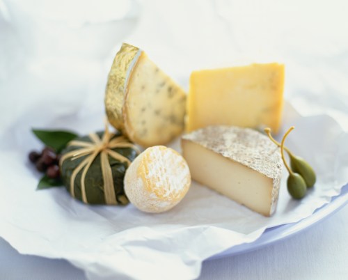 A selection of various cheeses arranged on white paper, accompanied by olives and herbs.