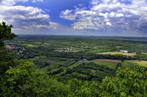 A panoramic view of lush green hills and fields under a cloudy blue sky.