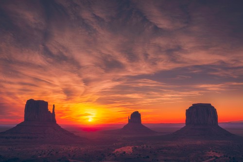 Sunset over Monument Valley, featuring iconic rock formations silhouetted against a colorful sky.