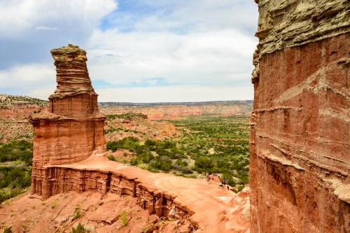 A scenic view of red rock formations and cliffs in a desert landscape under a cloudy sky.