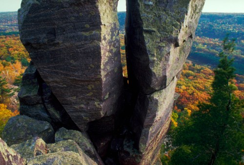 A split rock formation with vibrant autumn foliage in the background, showcasing a scenic landscape.