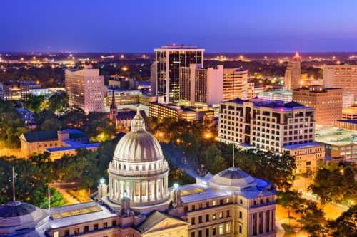 Aerial view of a city skyline at dusk, featuring illuminated buildings and a prominent dome in the foreground.