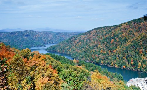 A scenic view of a river winding through colorful autumn foliage and rolling hills under a clear blue sky.