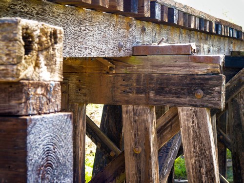 Close-up of weathered wooden beams and supports of a rustic bridge, showcasing textures and aged materials.