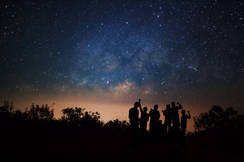 Silhouettes of people against a starry night sky, with the Milky Way visible in the background.