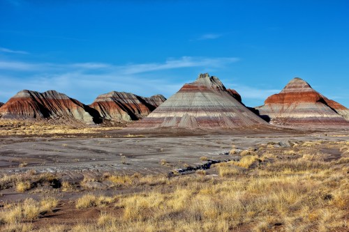 Colorful striped rock formations rise against a clear blue sky, surrounded by sparse grassland.