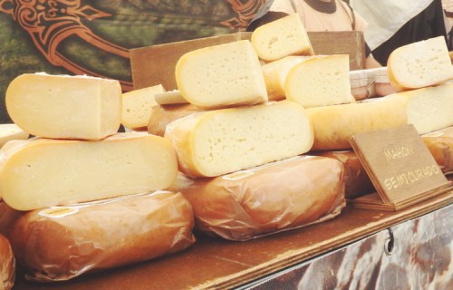A display of various cheese blocks wrapped in brown paper at a market stall.