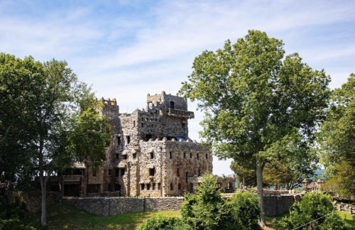 A stone castle with multiple towers surrounded by trees and a clear blue sky.