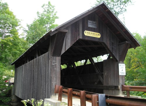 A wooden covered bridge surrounded by trees, featuring signs about weight limits and vehicle restrictions.