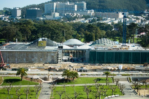 Construction site of a modern building surrounded by greenery and cityscape in the background.