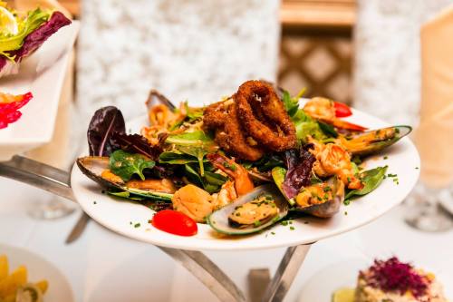 A vibrant seafood salad with shrimp, mussels, greens, cherry tomatoes, and crispy onion rings on a white plate.