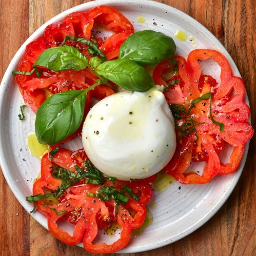A plate of sliced red tomatoes topped with fresh basil and a ball of creamy burrata drizzled with olive oil.