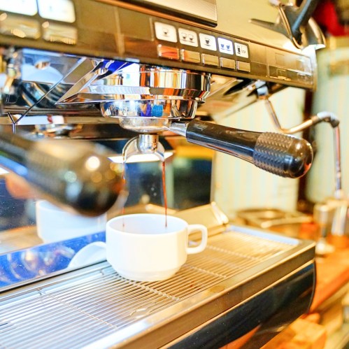 A close-up of an espresso machine brewing coffee into a white cup.