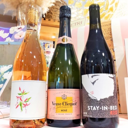 Three bottles of wine: a rosé, Veuve Clicquot champagne, and a red wine labeled "Stay In Bed."