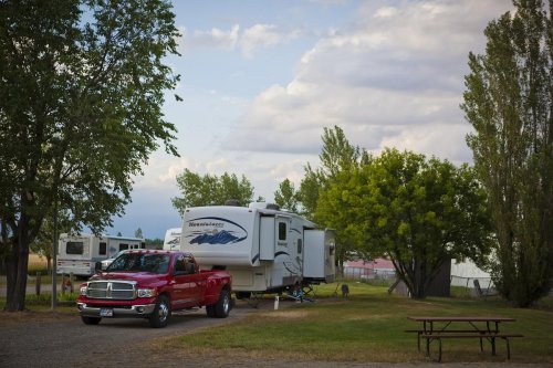 A red pickup truck parked next to a large RV in a grassy area with trees and a picnic table nearby.