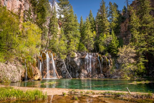 A serene landscape featuring a waterfall cascading into a clear pool, surrounded by lush green trees and rocky cliffs.