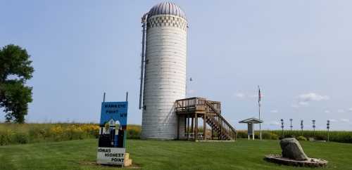 A tall white silo with a dome, next to a sign reading "Hawkeye Point," surrounded by green fields and a clear blue sky.