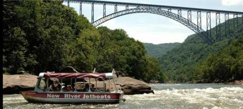 A jetboat navigates the New River, with a large bridge and lush green hills in the background.