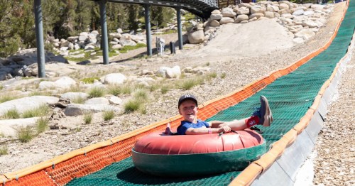 A child smiles while sliding down a grassy slope on a colorful inner tube.