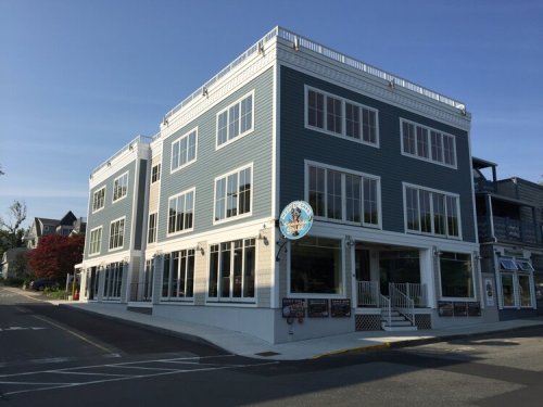 A modern, blue multi-story building with large windows and a sign, located on a sunny street.