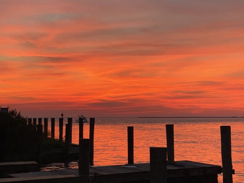 A vibrant sunset over calm waters, with silhouetted posts and a distant boat against a colorful sky.