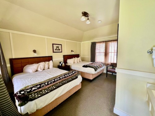 A cozy hotel room featuring two beds, a window with curtains, and warm lighting.