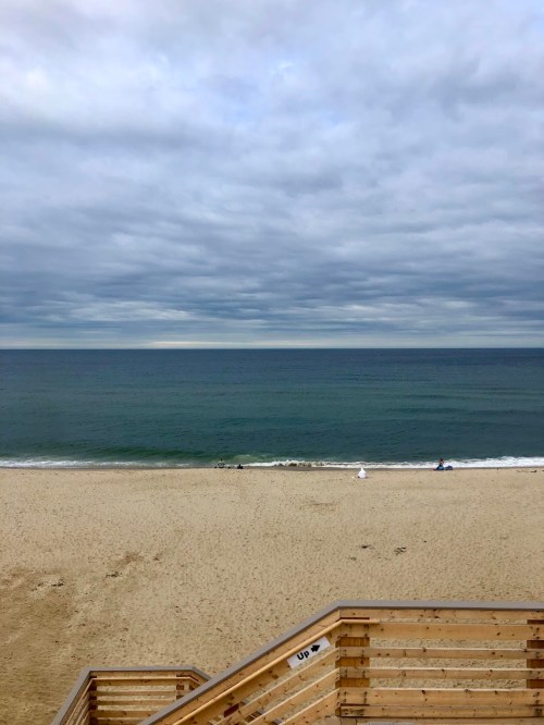 A sandy beach with gentle waves under a cloudy sky, featuring a few people in the distance.