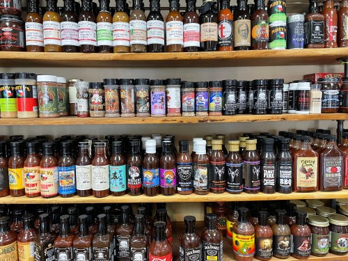 A variety of hot sauces and seasonings displayed on wooden shelves, showcasing colorful labels and diverse brands.