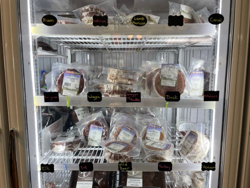 A refrigerator display filled with various packaged meats, including bison, ostrich, lamb, duck, and more.