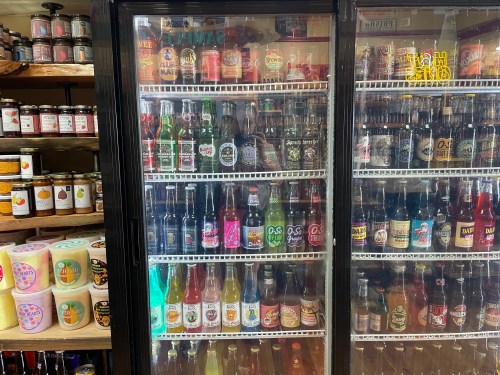 A refrigerator filled with various colorful soda bottles and jars on shelves in a store.