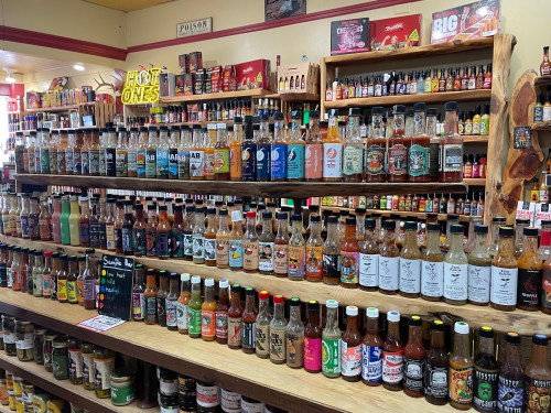 A colorful display of various hot sauces on wooden shelves in a store, showcasing numerous brands and flavors.