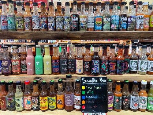 A display of various hot sauce bottles arranged on shelves, with a sign indicating heat levels: low, mild, medium, hot.