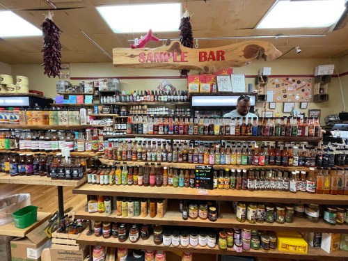A vibrant store interior featuring shelves of sauces and condiments, with a "Sample Bar" sign above.