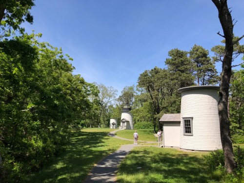 A path leads through greenery to several white, round buildings under a clear blue sky.