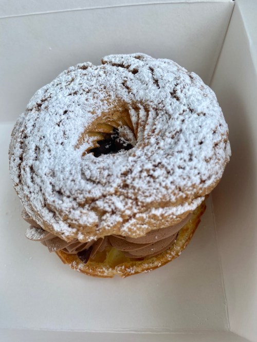 A round pastry topped with powdered sugar, filled with chocolate cream, presented in a white box.