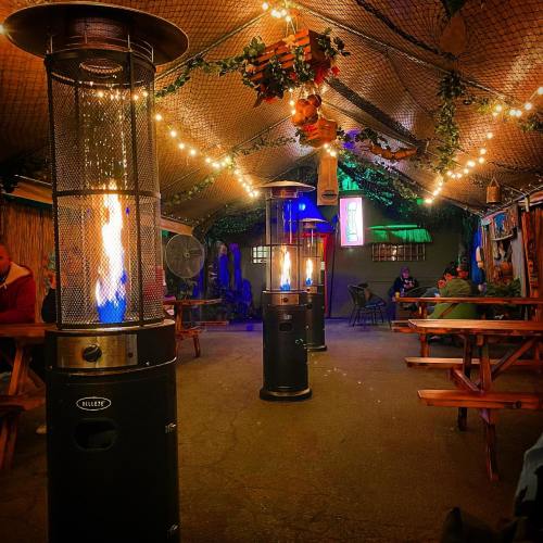 Cozy indoor space with gas heaters, string lights, and wooden tables, creating a warm atmosphere for guests.