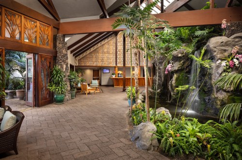 A tropical lobby with wooden accents, lush plants, and a waterfall feature, creating a serene atmosphere.