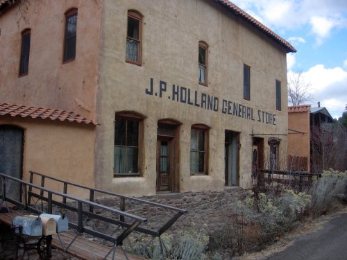 Historic J.P. Holland General Store building with a rustic facade and a sloped ramp, surrounded by sparse vegetation.