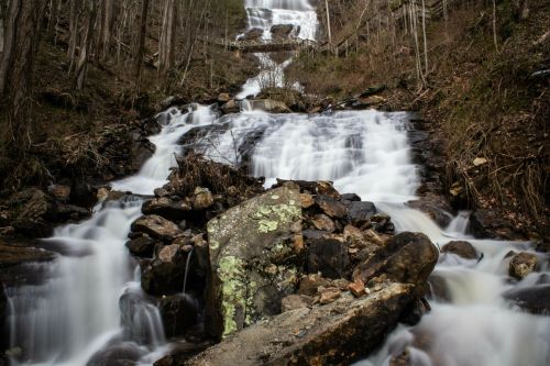 A cascading waterfall flows over rocks, surrounded by trees in a serene natural setting.
